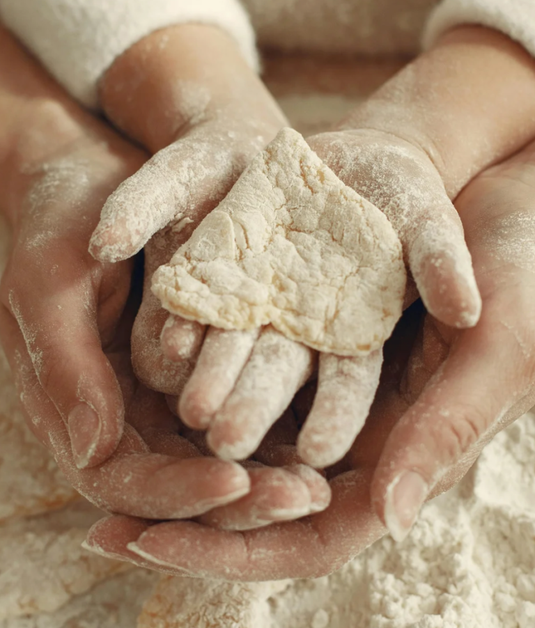 Adult hand holding a Childs hand with a biscuit heart and floury hands